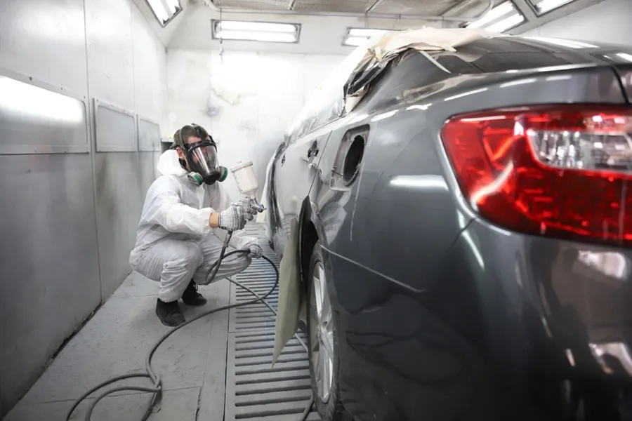 Technician spray painting a car panel